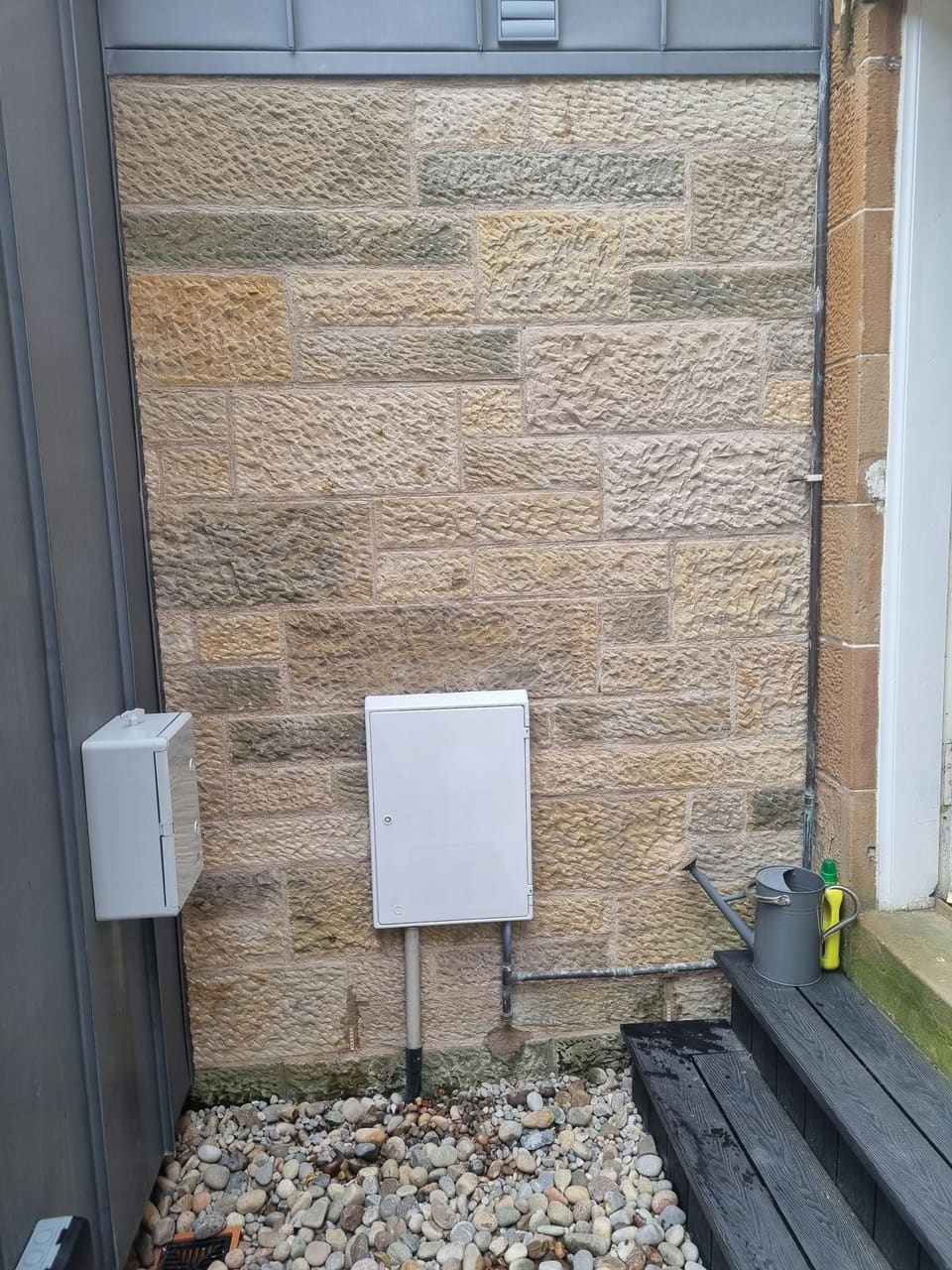 Panel of squared and snecked sandstone with tooled faces and fine joints, built against a modern clad wall.