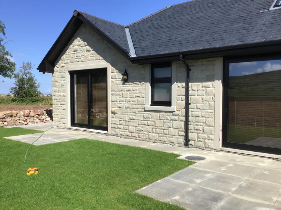 New house in squared buff sandstone with dressed margins to the openings, under a slate roof.