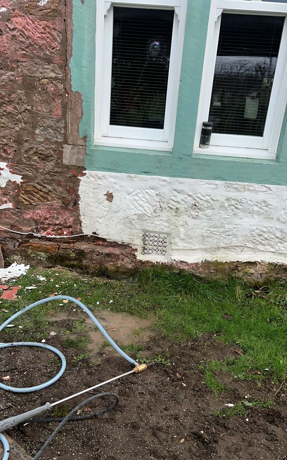 Lance and hoses on the grass below a double window with green-painted margins. Stone to the left is stripped; the base is still white.