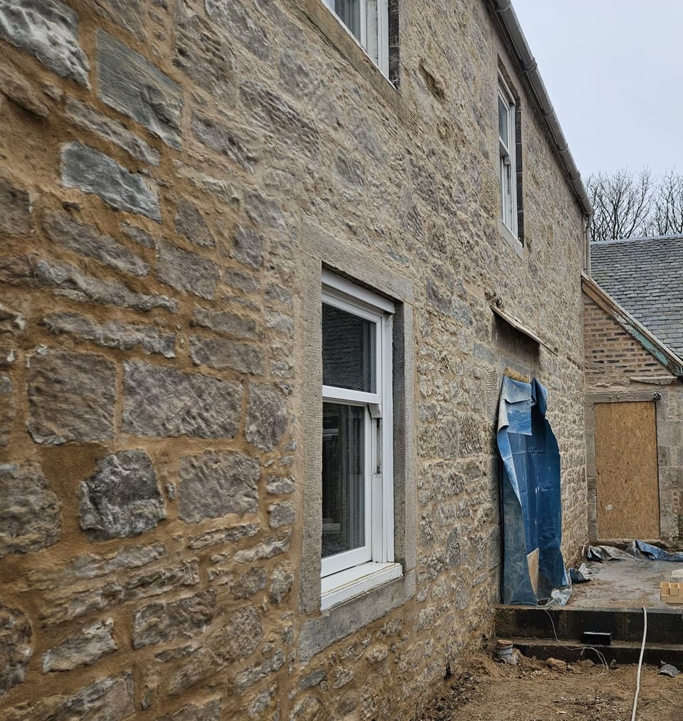 Looking along the repointed rubble wall. Buff lime mortar fills the joints close to the stone faces around a window with dressed margins.