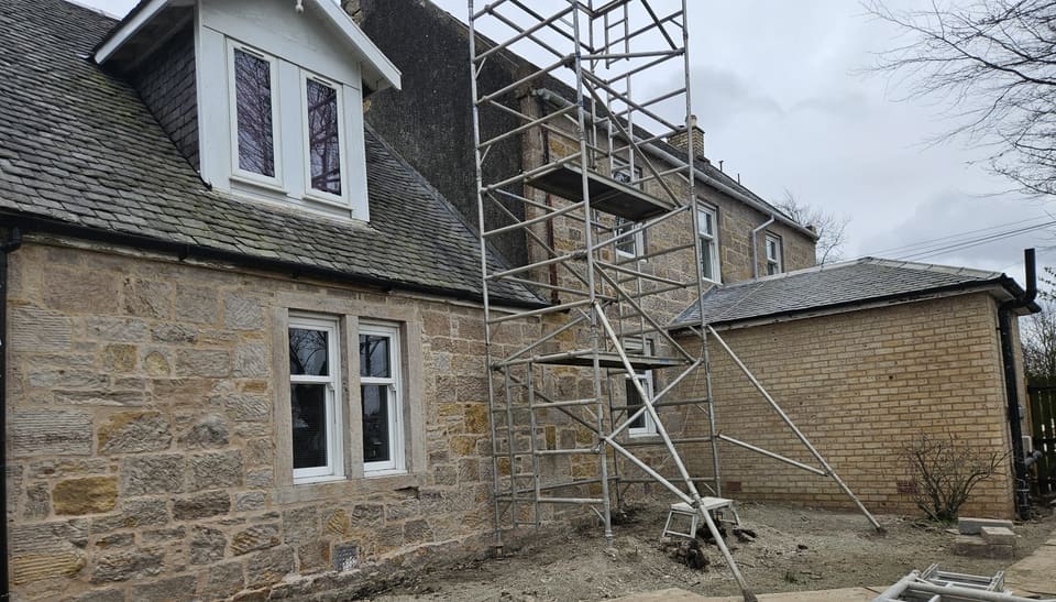 Wing with a white dormer in a slate roof, its sandstone cleaned and repointed.