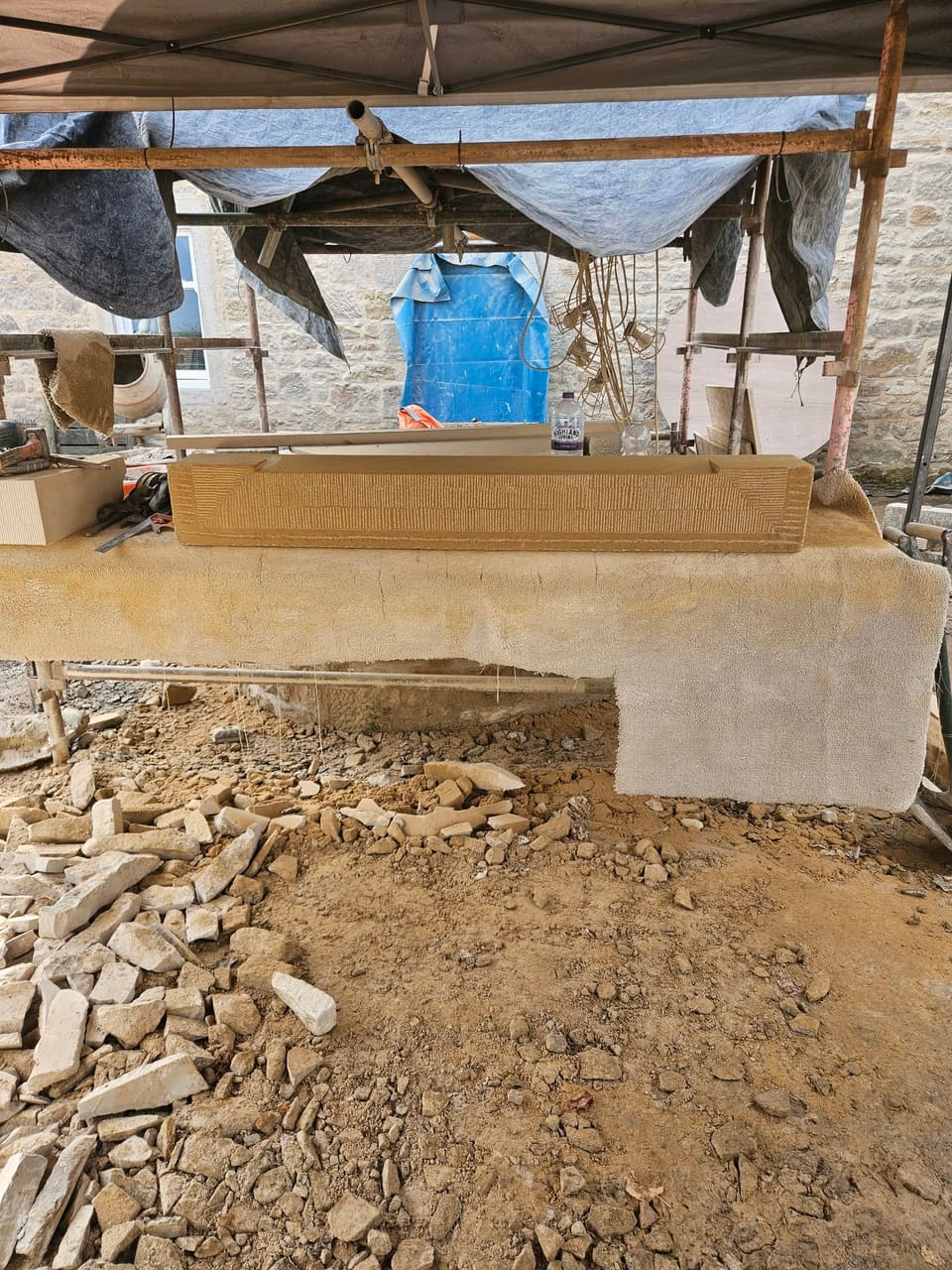 Sandstone sill on a sacking-covered banker under a sheeted scaffold, stone chippings on the ground.