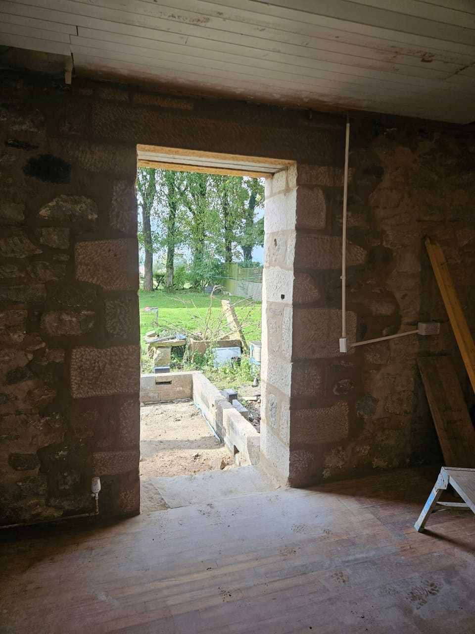 Inside view through the new back doorway, dressed stone at the reveal, trees beyond.
