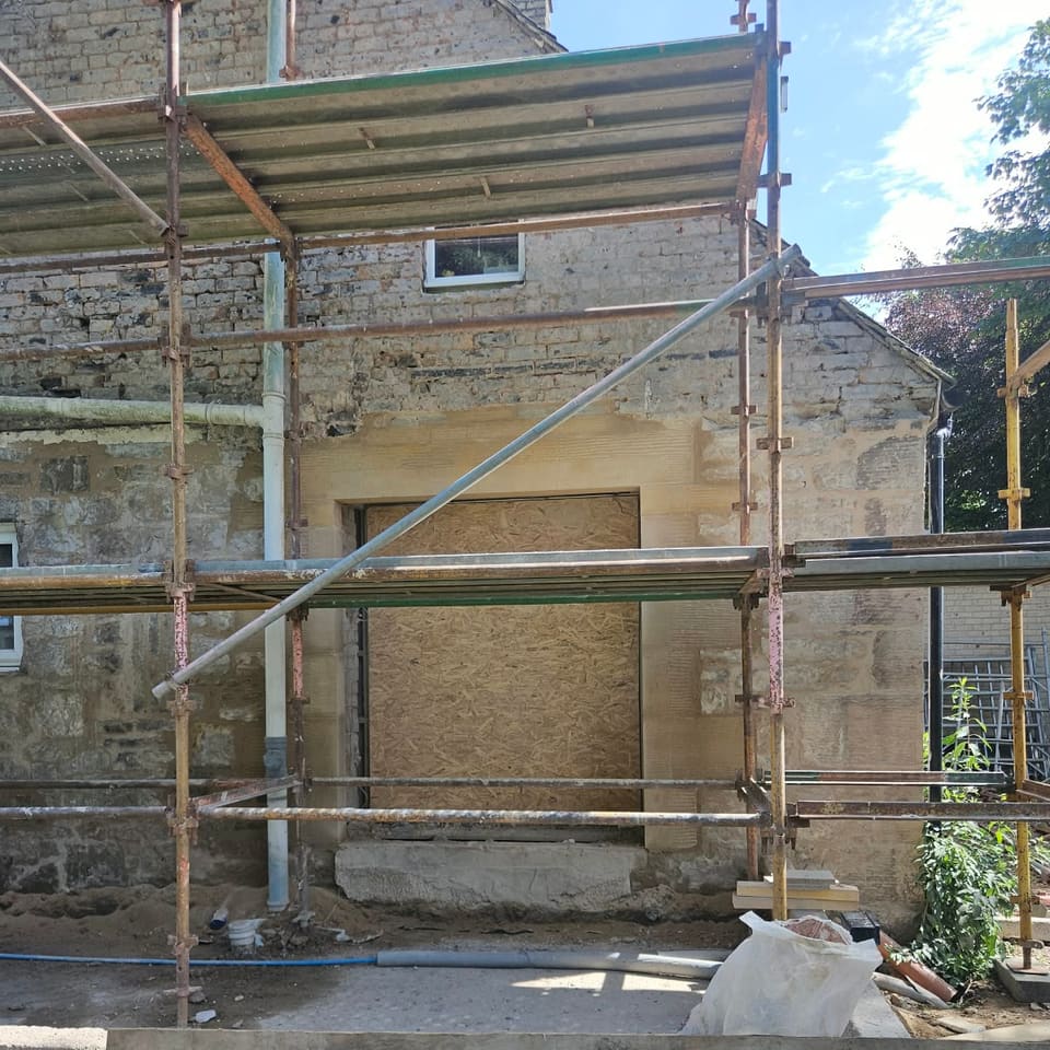 Wide opening boarded with OSB behind a scaffold, framed by new sandstone rybats and a long lintel.