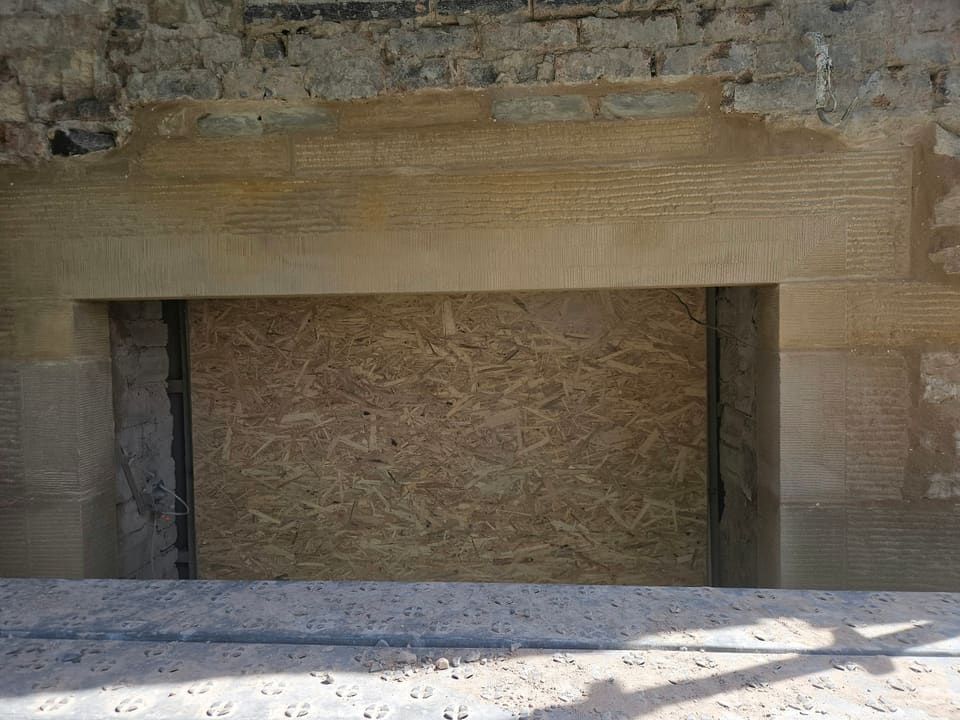 Close view of the long sandstone lintel over a wide boarded opening, rybats either side.