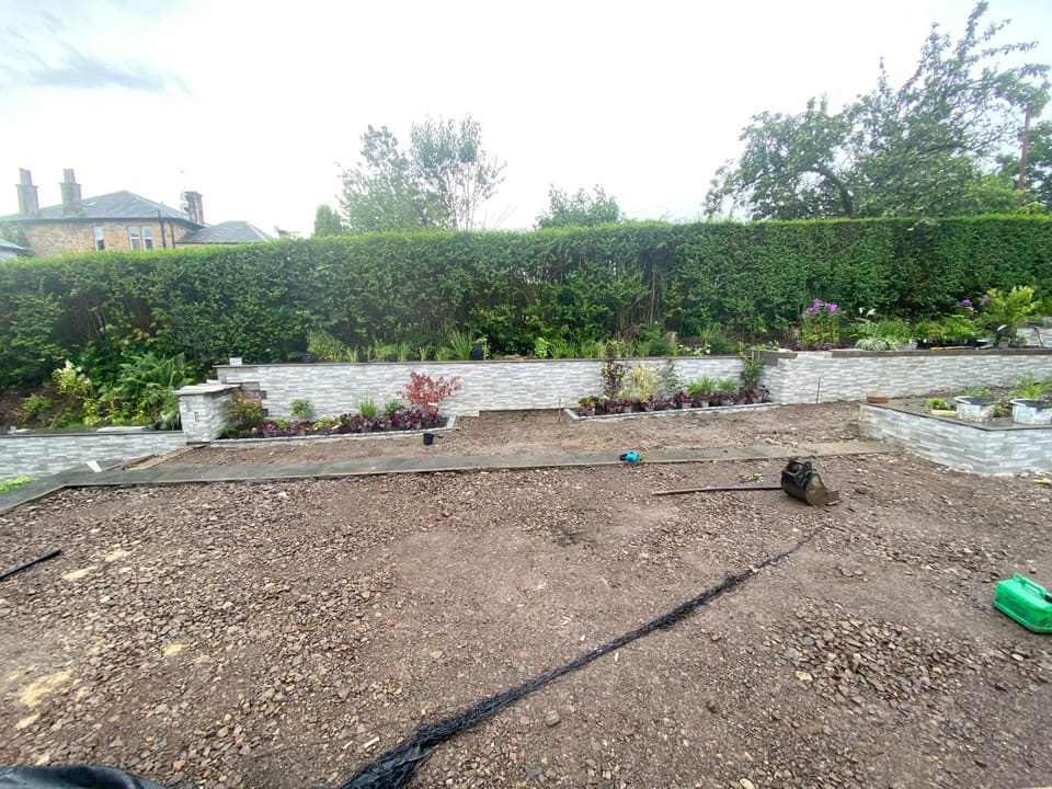 Clad retaining walls with slab copings along the back of the garden, planted up, with the ground in front levelled.
