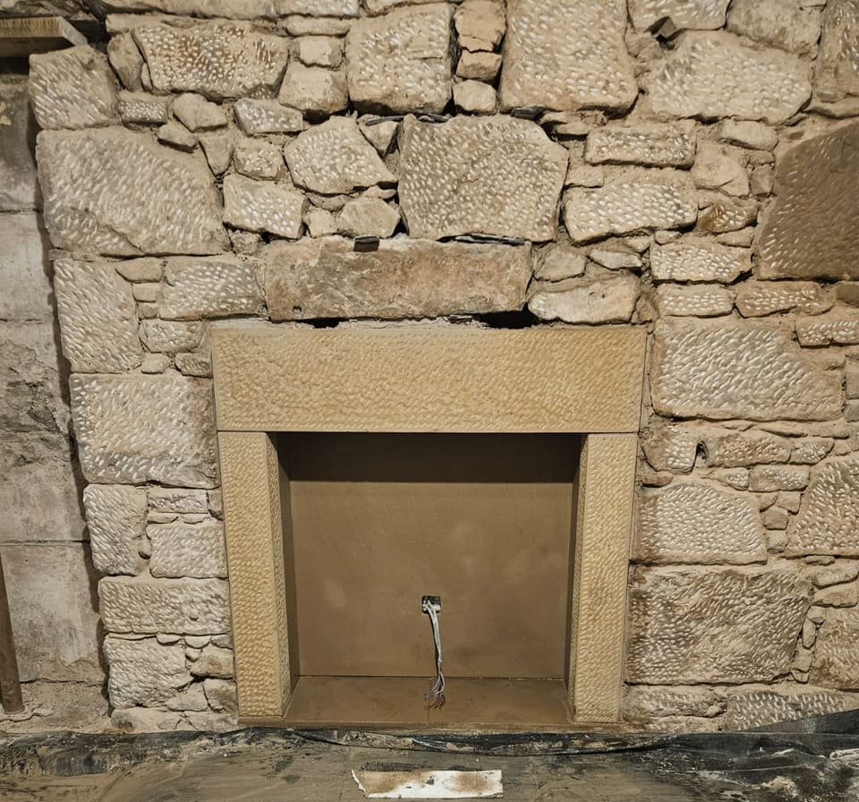 New dressed sandstone fireplace surround built into a rubble stone wall with tooled faces, the opening inside lined.