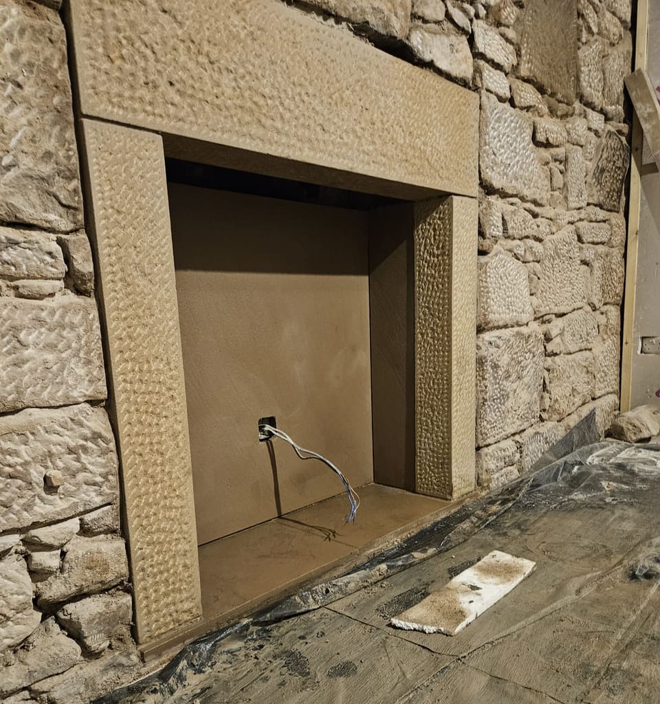 Close view of the new fireplace surround in dressed buff sandstone, its textured face set against the old stone wall.