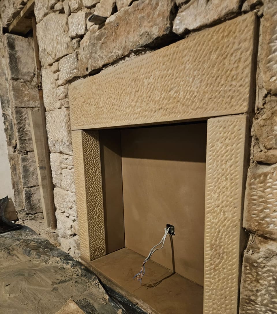The new sandstone fireplace surround seen from the left, its lintel and side stones worked with a textured face.