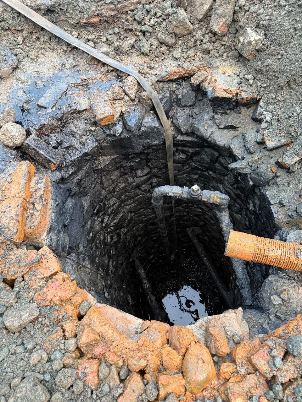 Shaft with the water pumped down: black-coated rubble lining, old iron pipe with elbow and valve, cross-members near the bottom.