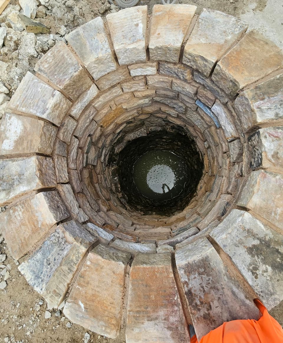 Straight down on a ring of tapered coping stones with open radial joints and water at the bottom of the shaft.