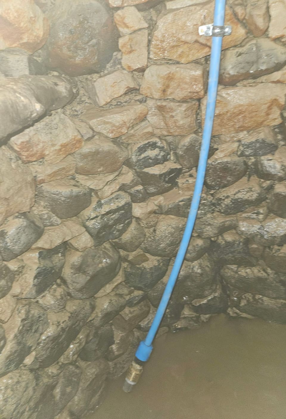 The foot of the blue pipe, with a brass fitting on the end, clipped to the original rubble lining down at the water.